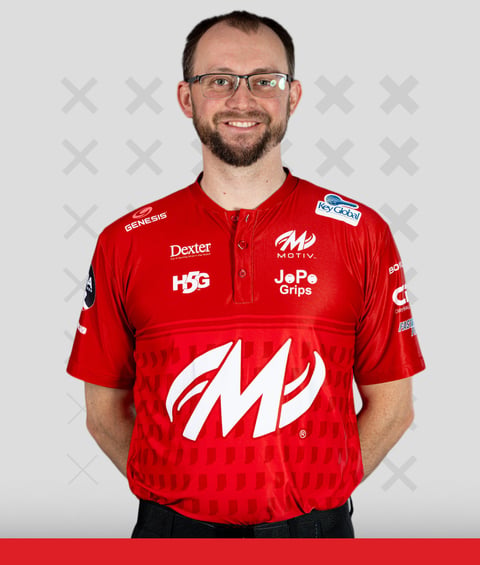 Man wearing red bowling shirt with sponsor logos smiling at camera against gray background
